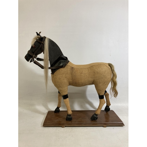 42 - A VINTAGE WOODEN AND BURLAP HORSE ON A WOODEN BASE WITH LEATHER EARS AND BRIDLE