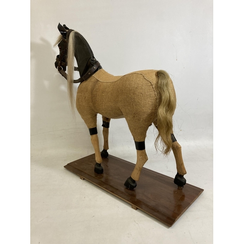 42 - A VINTAGE WOODEN AND BURLAP HORSE ON A WOODEN BASE WITH LEATHER EARS AND BRIDLE