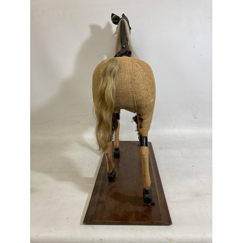 42 - A VINTAGE WOODEN AND BURLAP HORSE ON A WOODEN BASE WITH LEATHER EARS AND BRIDLE