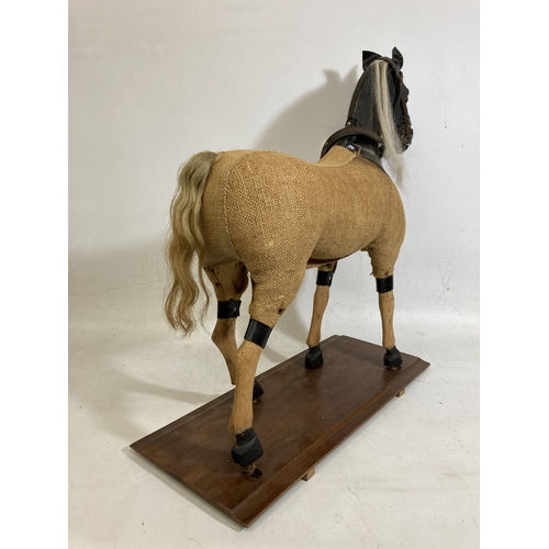 42 - A VINTAGE WOODEN AND BURLAP HORSE ON A WOODEN BASE WITH LEATHER EARS AND BRIDLE