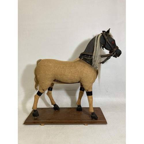 42 - A VINTAGE WOODEN AND BURLAP HORSE ON A WOODEN BASE WITH LEATHER EARS AND BRIDLE