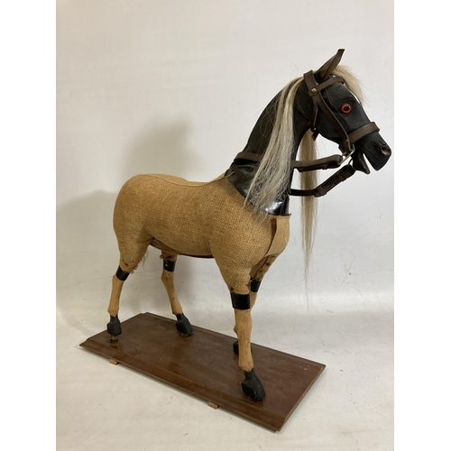 42 - A VINTAGE WOODEN AND BURLAP HORSE ON A WOODEN BASE WITH LEATHER EARS AND BRIDLE