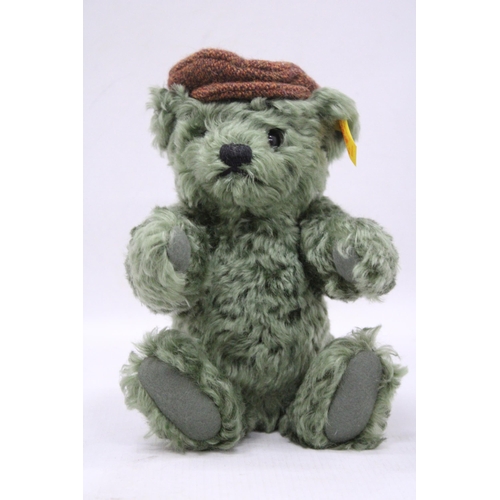 108 - A SMALL GREEN STEIFF THURSDAY TEDDY BEAR WITH A FLAT CAP AND BUTTON TO HIS EAR, HEIGHT 25CM