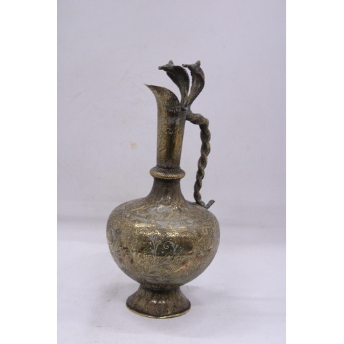 79 - A DECORATIVE BRASS JUG WITH A LONG SPOUT AND AN ORNATE HANDLE IN THE FORM OF A PAIR OF COBRA'S