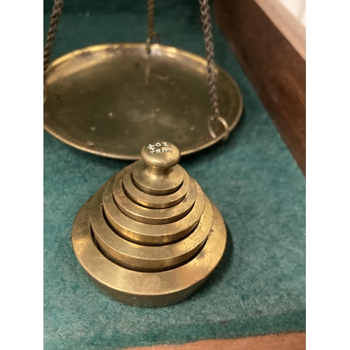 74 - A PAIR OF BRASS BALANCE SCALES IN A GLASS CASE WITH WEIGHTS TO INCLUDE TROY OZ, DWTS AND A 4 GRAIN W... 