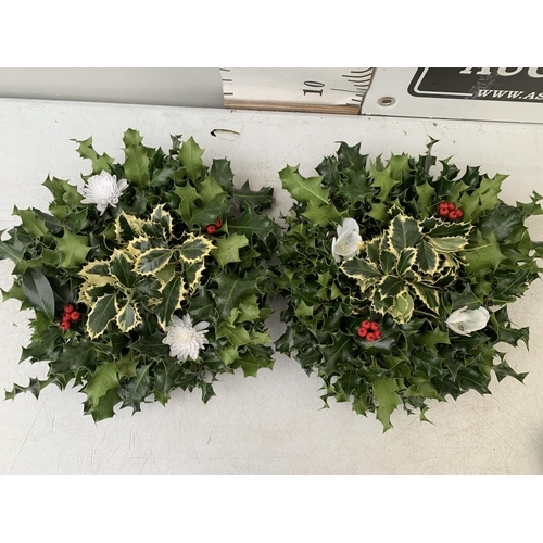 25 - TWO CHRISTMAS WREATHS WITH HOLLY, RIBBON AND CHRISTMAS ACCESSORIES ON A MOSS RING. APPROX 30CM IN DI... 