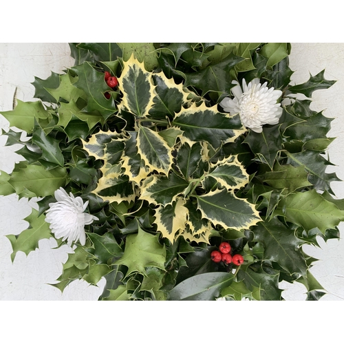 25 - TWO CHRISTMAS WREATHS WITH HOLLY, RIBBON AND CHRISTMAS ACCESSORIES ON A MOSS RING. APPROX 30CM IN DI... 