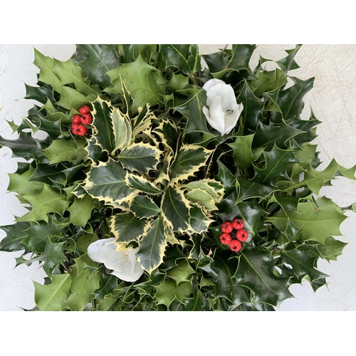 25 - TWO CHRISTMAS WREATHS WITH HOLLY, RIBBON AND CHRISTMAS ACCESSORIES ON A MOSS RING. APPROX 30CM IN DI... 