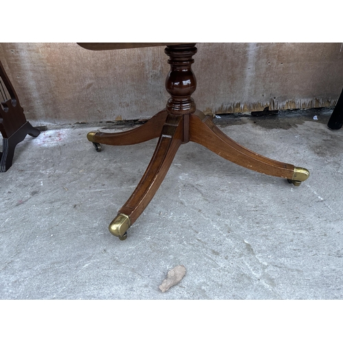 2996 - AN OVAL MAHOGANY COFFEE TABLE WITH INSET LEATHER TOP ON PEDESTAL BASE WITH BRASS CASTERS 48