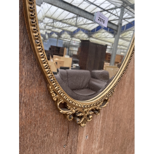 2976 - AN OVAL GILT FRAMED BEVEL EDGE WALL MIRROR WITH FOLIATE FRAME, 26