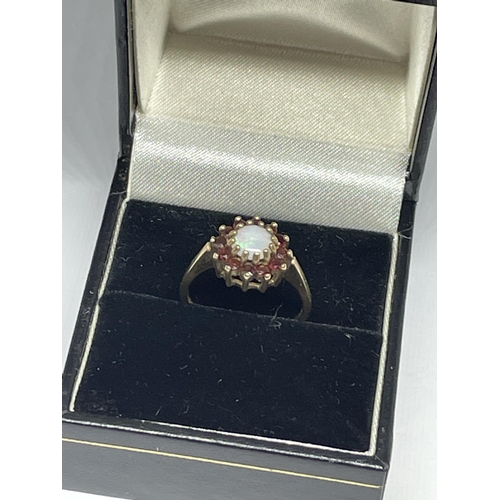 511 - A 9 CARAT YELLOW GOLD RING WITH CENTRE OPAL SURROUNDED BY GARNETS IN A FLOWER DESIGN SIZE M IN A PRE... 