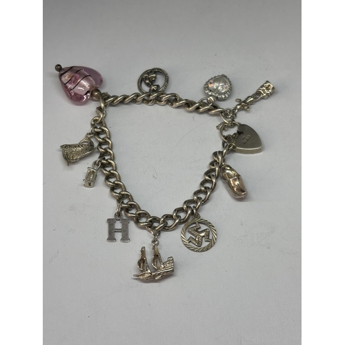 523 - A MARKED SILVER CHARM BRACELET WITH TEN CHARMS AND A HEART PADLOCK