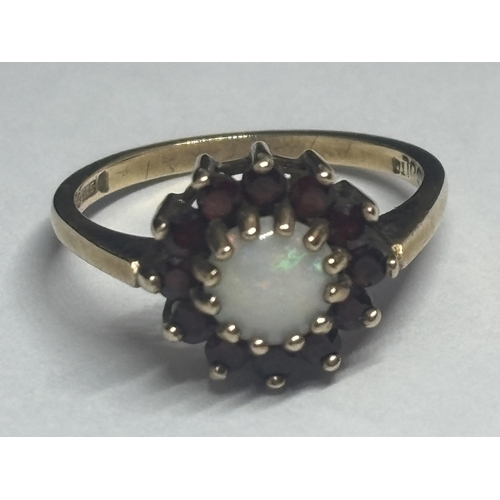 605 - A 9 CARAT YELLOW GOLD RING WITH CENTRE OPAL SURROUNDED BY GARNETS IN A FLOWER DESIGN SIZE M IN A PRE... 