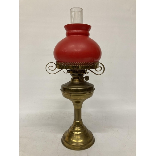 65 - A VINTAGE BRASS OIL LAMP WITH RED GLASS SHADE AND CHIMNEY, HEIGHT APPROX 55CM