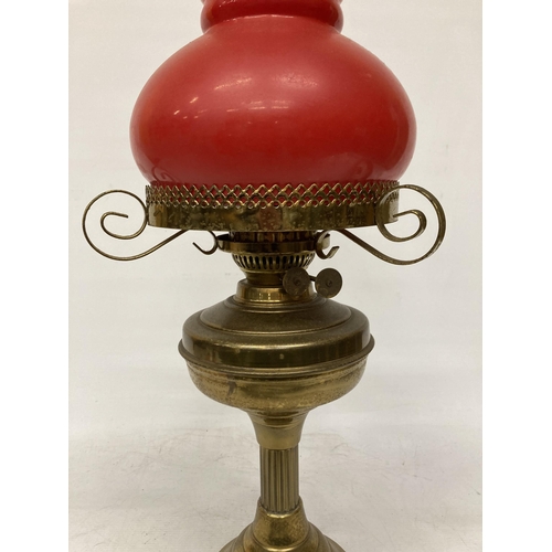 65 - A VINTAGE BRASS OIL LAMP WITH RED GLASS SHADE AND CHIMNEY, HEIGHT APPROX 55CM