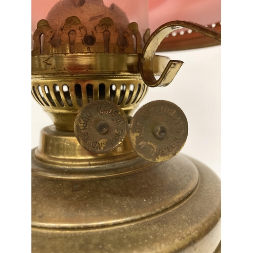 65 - A VINTAGE BRASS OIL LAMP WITH RED GLASS SHADE AND CHIMNEY, HEIGHT APPROX 55CM