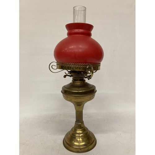 65 - A VINTAGE BRASS OIL LAMP WITH RED GLASS SHADE AND CHIMNEY, HEIGHT APPROX 55CM