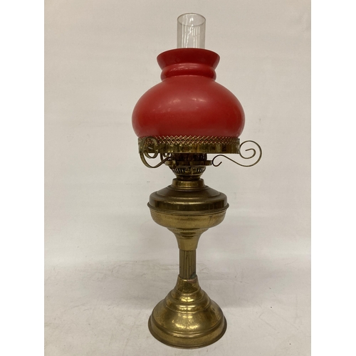 65 - A VINTAGE BRASS OIL LAMP WITH RED GLASS SHADE AND CHIMNEY, HEIGHT APPROX 55CM