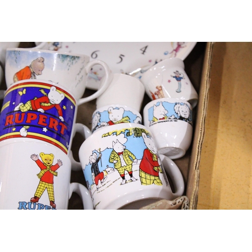 424 - A COLLECTION OF RUPERT THE BEAR ITEMS TO INCLUDE CUPS, A CERAMIC WALL CLOCK, EGG CUPS, TWO FRAMED JI... 