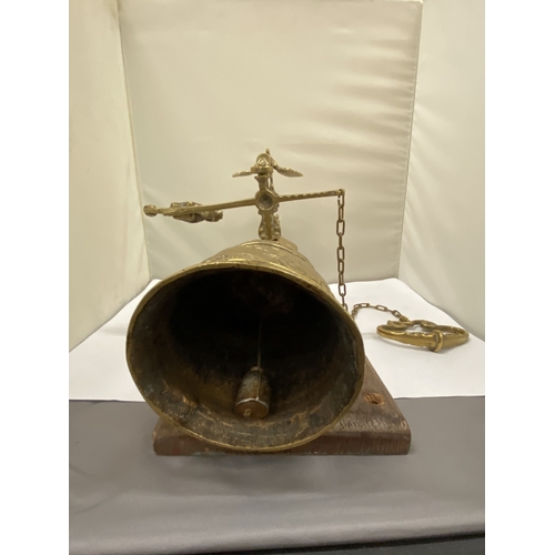 26 - A VINTAGE BRASS BELL ON AN ORNATE BRACKET AND WOODEN PLINTH