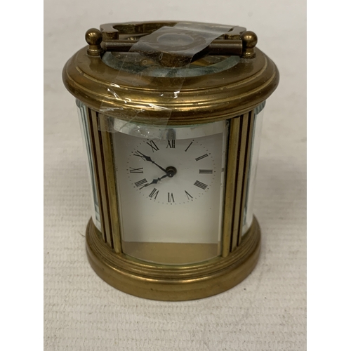 31 - A SMALL OVAL BRASS CARRIAGE CLOCK WITH GLASS ESCAPEMENT AND KEY