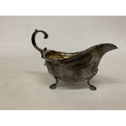 1 - A 1930'S HALLMARKED BIRMINGHAM SILVER SAUCE BOAT WITH A WAVY EDGE RIM AND RAISED ON THREE ORNATE FEE... 