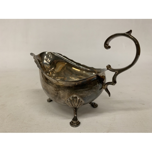 1 - A 1930'S HALLMARKED BIRMINGHAM SILVER SAUCE BOAT WITH A WAVY EDGE RIM AND RAISED ON THREE ORNATE FEE... 