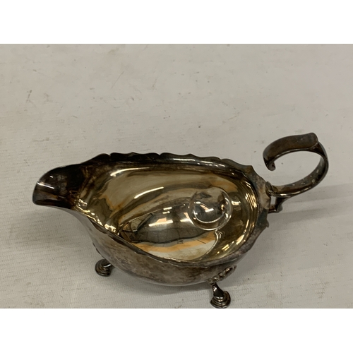 1 - A 1930'S HALLMARKED BIRMINGHAM SILVER SAUCE BOAT WITH A WAVY EDGE RIM AND RAISED ON THREE ORNATE FEE... 