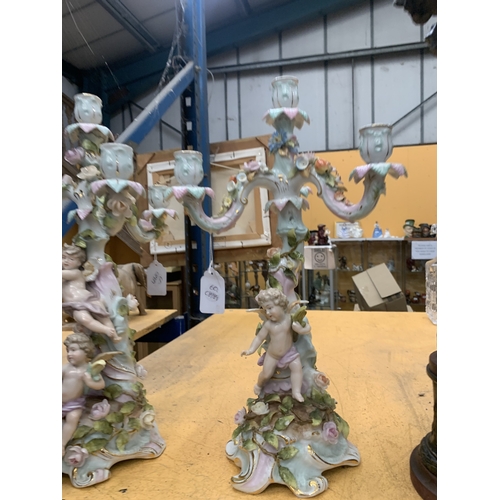 51 - A PAIR OF GERMAN PORCELAIN FIGURAL CANDELABRAS WITH A CHERUB FIGURAL DESIGN AND FLORAL ENCRUSTATIONS... 