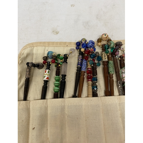 55 - A COLLECTION OF 34 LACE MAKING BOBBINS, MANY WITH ENAMEL DECORATION, CHARMS AND SPANGLES IN A CLOTH ... 
