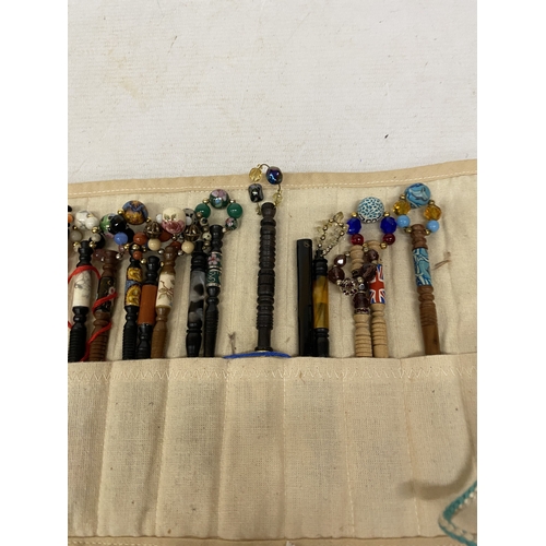 55 - A COLLECTION OF 34 LACE MAKING BOBBINS, MANY WITH ENAMEL DECORATION, CHARMS AND SPANGLES IN A CLOTH ... 