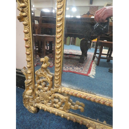 566 - AN EARLY 19TH CENTURY GILT AND COMPOSITION WALL MIRROR, the scrolling Rococo style surmount above tw... 