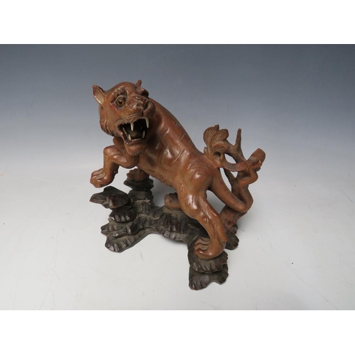 519 - A 20TH CENTURY JAPANESE CARVED HARDWOOD TIGER, on a naturalistic wood base, H 19.5 cm, W 18 cm