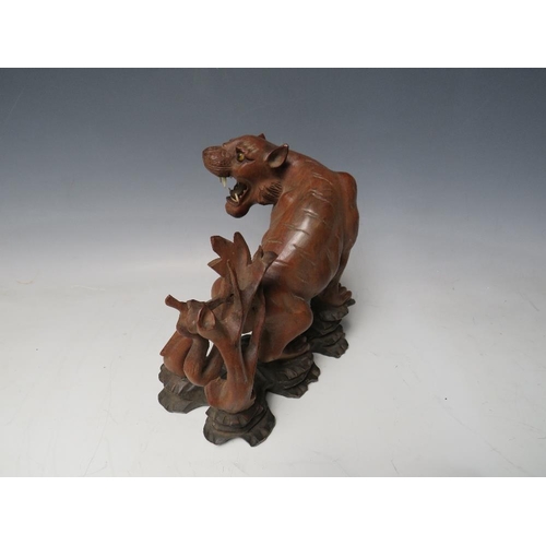 519 - A 20TH CENTURY JAPANESE CARVED HARDWOOD TIGER, on a naturalistic wood base, H 19.5 cm, W 18 cm