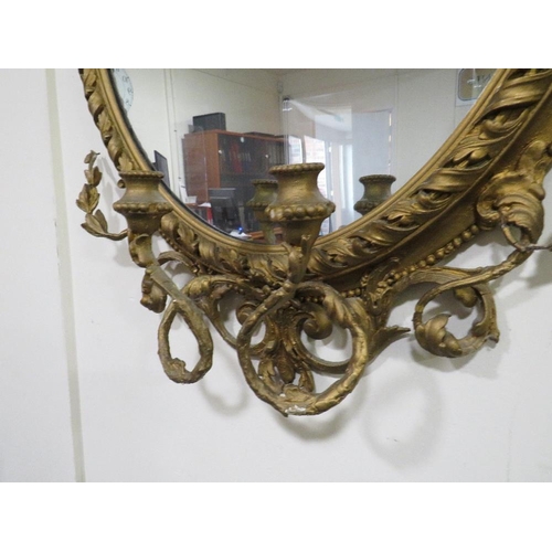 631 - A 19TH CENTURY LARGE GILT OVAL WALL MIRROR WITH TWIN CANDLE SCONCE, having a scrolling foliate detai... 