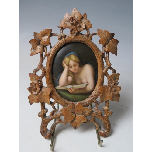 67 - A 19TH CENTURY CONTINENTAL OVAL PORCELAIN PLAQUE OF A LADY READING, unsigned in a carved wooden fram... 
