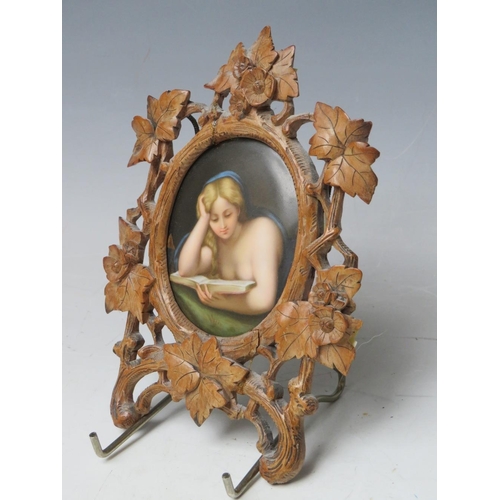 67 - A 19TH CENTURY CONTINENTAL OVAL PORCELAIN PLAQUE OF A LADY READING, unsigned in a carved wooden fram... 