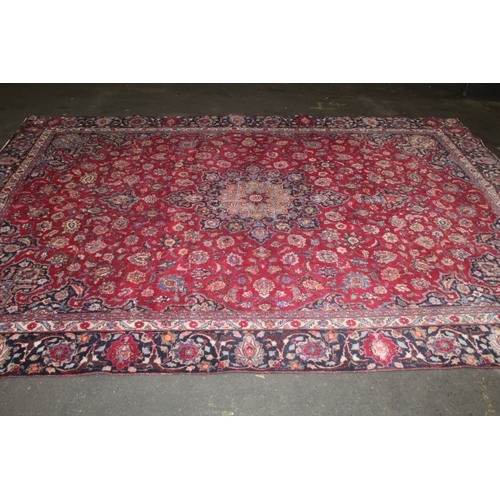 849 - A LARGE EASTERN WOOLLEN RUG IN MAINLY RED AND BLACK PATTERN 377 X 275 CM