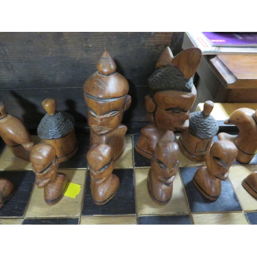 103 - A CARVED WOODEN CHESS SET AND BOARD DEPICTING AFRICAN STYLISED PIECES