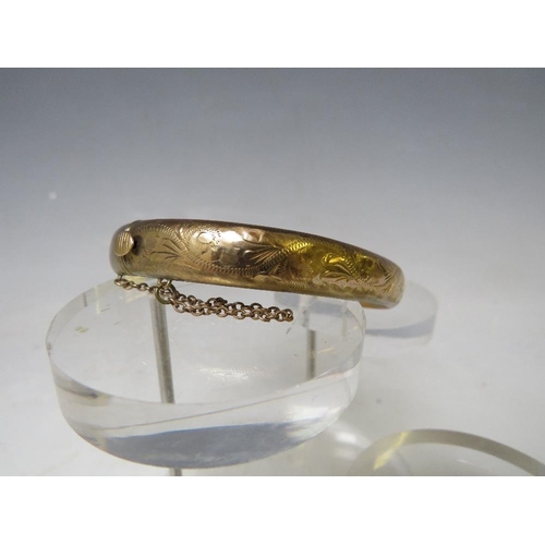 146 - A HALLMARKED 9CT GOLD HINGED BANGLE, with engraved embellishment to one side and with safety chain, ... 