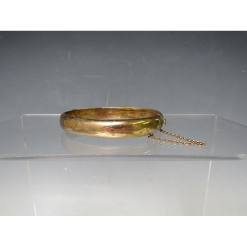 146 - A HALLMARKED 9CT GOLD HINGED BANGLE, with engraved embellishment to one side and with safety chain, ... 