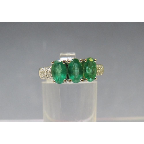 157 - AN 18CT WHITE GOLD 'ILIANA' THREE STONE EMERALD RING, with diamond chip set shoulders, ring size O t... 