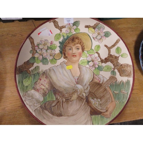 137 - A LARGE CERAMIC CHARGER DECORATED WITH A LADY PICKING FLOWERS