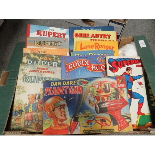 142 - Two trays of vintage games and annuals to include a vintage Dan Dare planet gun in original box