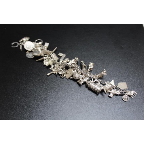 627 - A HEAVY SILVER CHARM BRACELET, festooned with many charms, approx weight 107.6g