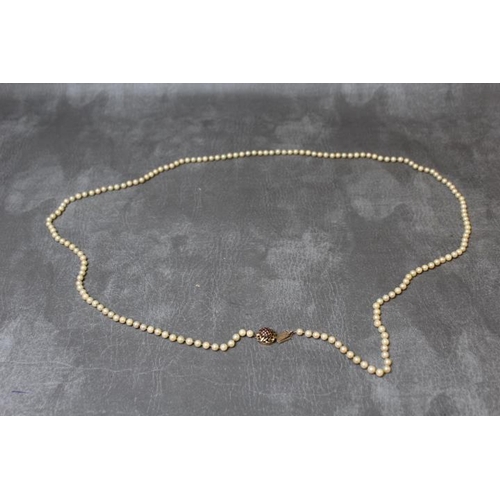 672 - A LONG STRAND OF INDIVIDUALLY KNOTTED FRESHWATER CULTURED PEARLS ON A DOMED 9ct GARNET SET FASTENING... 