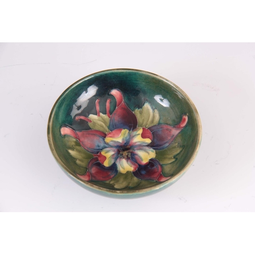 36 - A CIRCA 1950S WALTER MOORCROFT COLUMBINE PATTERN FOOTED BOWL on a green ground 4cm high, 11.5 cm dia... 