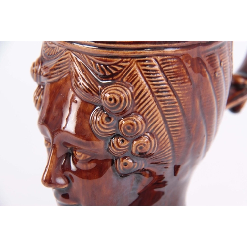 64 - A 19TH CENTURY TREACLE GLAZED POTTERY MUG moulded in the form of a ladies head, 15cm high by 16cm wi... 