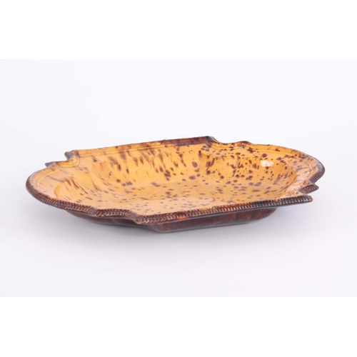 73 - AN 18TH CENTURY POTTERY DISH having treacle and yellow ochre splash decoration with ogee corners and... 