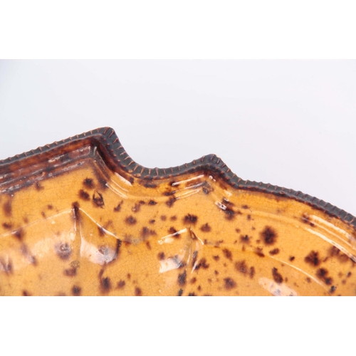 73 - AN 18TH CENTURY POTTERY DISH having treacle and yellow ochre splash decoration with ogee corners and... 